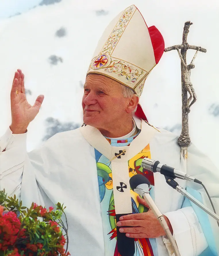 João Paulo II com vestes litúrgicas, mitra e báculo, com a mão direita levantada.